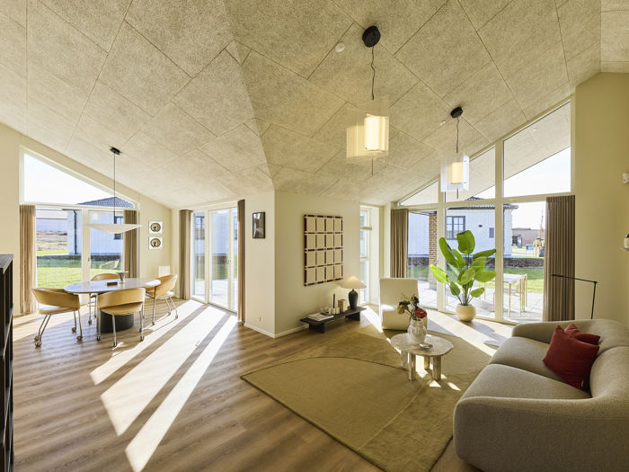 Åbent opholdsrum fra eurodan-huse med stue og spiseplads i samme rum, store vinduespartier, skrå akustiklofter, lys sofa, rundt sofabord, grøn plante og spisebord ved terrassedøren – inspiration til nybyggeri og husdrømme med sammenhængende køkken-alrum.