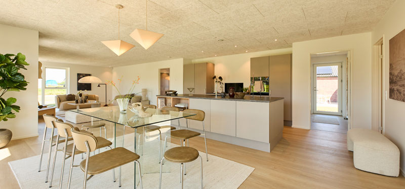 Spiseplads i køkken-alrum fra eurodan-huse med glasbord, brune spisebordsstole, lyse pendler, stor køkkenø, beige køkkenfronter og åben forbindelse til stuen – inspiration til nybyggeri og husdrømme.