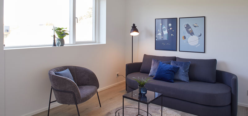 Lyst multirum med mørk sofa, lænestol, runde sofaborde og stort vindue – en hyggelig indretning med inspiration til moderne nybyggeri.