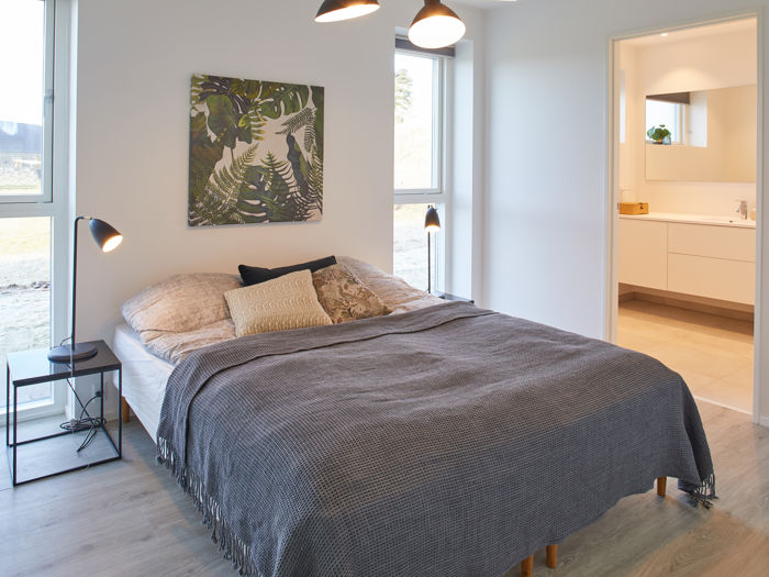 Lyst soveværelse med dobbeltseng, store gulv-til-loft-vinduer og direkte adgang til eget badeværelse – moderne inspiration til nyt hus og nybyggeri.