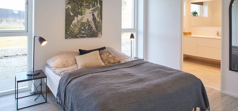 Lyst soveværelse med dobbeltseng, store gulv-til-loft-vinduer og direkte adgang til eget badeværelse – moderne inspiration til nyt hus og nybyggeri.