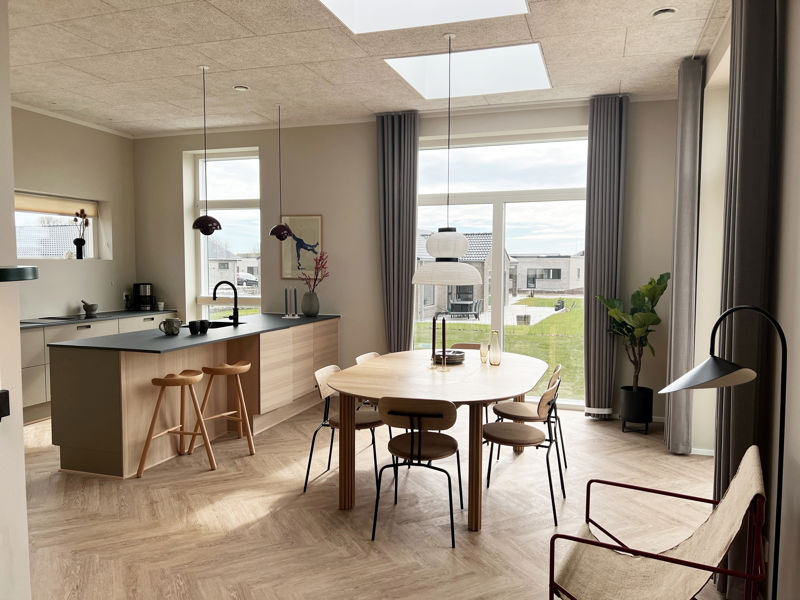 Lyst køkken-alrum fra eurodan-huse med køkkenø i træ, spiseplads, sildebensgulv, ovenlys og høje vinduespartier, der giver inspiration til moderne husdrømme.