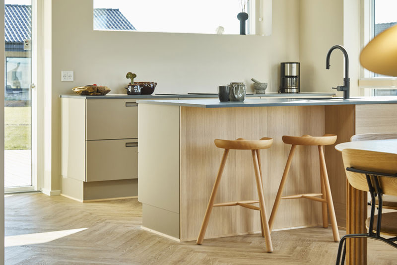 Detalje af moderne køkken i vinkelhus med køkkenø i træ, mørk bordplade, to barstole og sort armatur – inspiration til nybyg og drømmehuset.