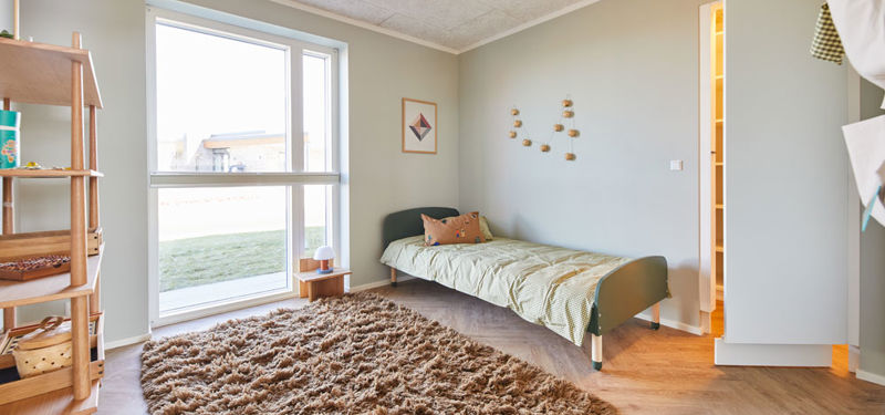Hyggeligt børneværelse i moderne vinkelhus med enkeltseng, stort vindue, blødt gulvtæppe og adgang til walk-in-closet – inspiration til indretning af nybyg og drømmehuset.