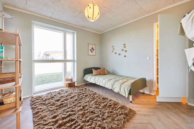 Hyggeligt børneværelse i moderne vinkelhus med enkeltseng, stort vindue, blødt gulvtæppe og adgang til walk-in-closet – inspiration til indretning af nybyg og drømmehuset.