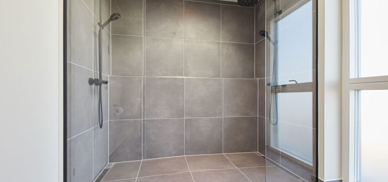 Rummelig dobbeltbruser i moderne vinkelhus med sorte glasvægge, to rainshowere, grå fliser og stort vinduesparti – inspiration til badeværelset i nybyg og drømmehuset.