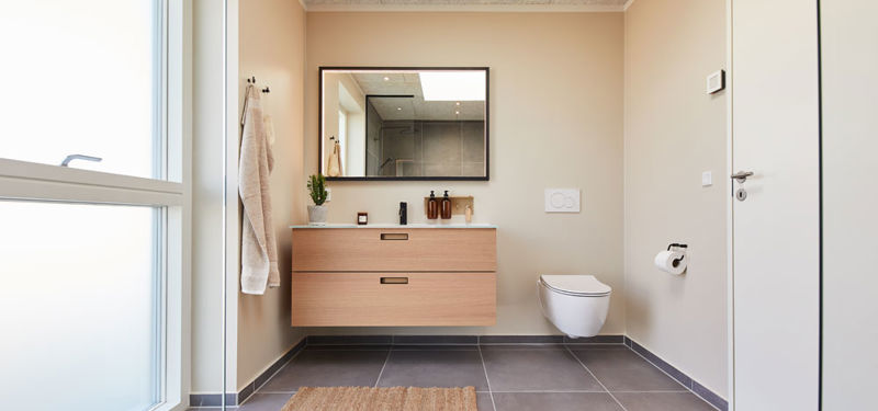 Moderne badeværelse i vinkelhus med svævende badmøbel i træ, stort spejl, væghængt toilet, mørke gulvfliser og stort vinduesparti – inspiration til nybyg og drømmehuset.