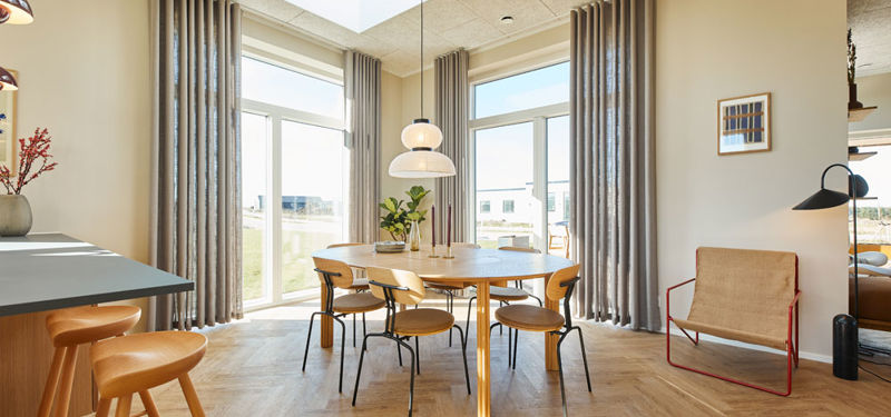 Lyst køkken-alrum i et moderne nybyggeri med rundt spisebord, store vinduespartier, ovenlys, lange gardiner og sildebensgulv.