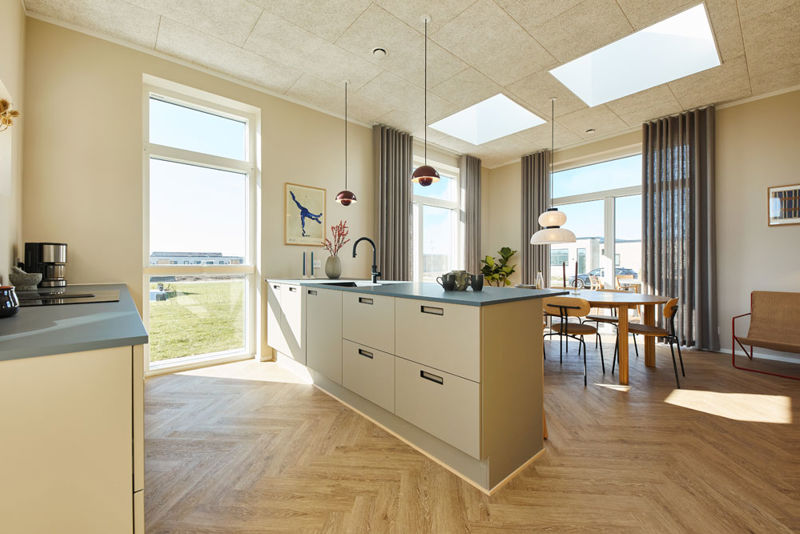 Lyst køkken-alrum i moderne vinkelhus med stor køkkenø, ovenlys, høje vinduespartier og spiseplads – inspiration til indretning af nybyg og drømmehuset.