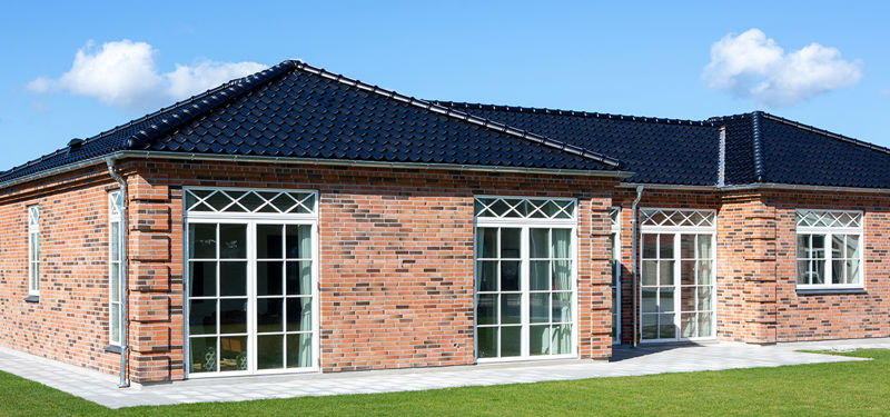 Facade fra eurodan-huse med røde mursten, sort tegltag, hvide sprossede vinduer, terrassedøre med glasfelter og flisegang langs huset – inspiration til palæstil, nybyggeri og husbyggeri med klassisk facadeudtryk.