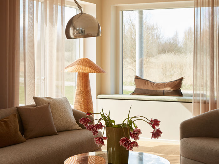 Hyggelig stue med beige sofaer, glasbord, buet gulvlampe, lange gardiner og en bred vindueskarm indrettet som siddeplads – stemningsfuld inspiration til moderne nybyg og husdrømme.