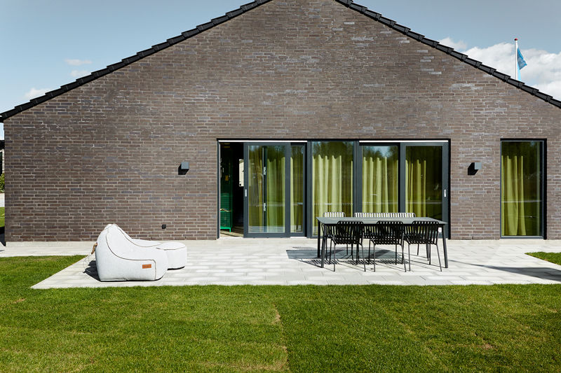 Bred terrasse foran murstensfacade fra eurodan-huse med store skydedøre, sorte udendørslamper, spisebord med mørke stole, loungepuf på flisebelægning og grøn plæne i forgrunden – inspiration til funktionelt nybyggeri og udeliv tæt på hjemmet.