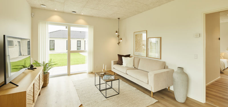 Lys stue med beige sofa, tv-møbel i træ, sorte sofaborde, stort gulvtæppe og brede glasdøre mod haven – indbydende inspiration til moderne nybyg og husdrømme.