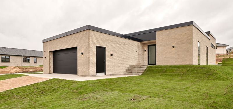 Moderne funkishus i lyse mursten med fladt tag, integreret garage og niveauforskudt grund – inspiration til nybyggeri med eurodan-huse.