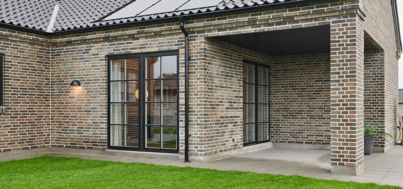 Moderne murstenshus med solceller, sorte glasdøre og overdækket terrasse – inspiration til nybyggeri.
