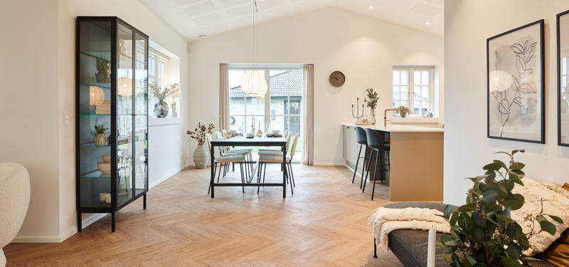 Åbent opholdsrum fra eurodan-huse med sildebensgulv, sort vitrineskab, spiseplads med pendellampe, køkkenø med barstole og hyggelig siddeplads i forgrunden – inspiration til nybyggeri, palæstil og sammenhængende husdrømme.