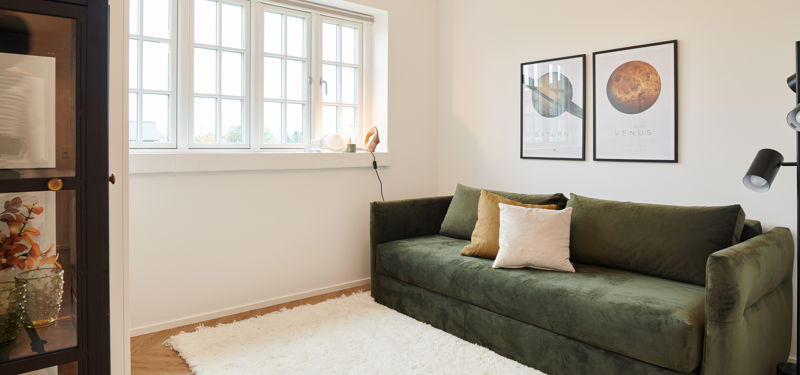 Stue eller værelse fra eurodan-huse med sprosset vindue, dyb grøn sofa, hvidt tæppe, sort vitrineskab, væglampe og planetplakater på væggen – inspiration til nybyggeri, husbyggeri og indretning af lyse opholdsrum.