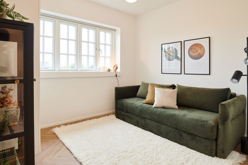 Stue eller værelse fra eurodan-huse med sprosset vindue, dyb grøn sofa, hvidt tæppe, sort vitrineskab, væglampe og planetplakater på væggen – inspiration til nybyggeri, husbyggeri og indretning af lyse opholdsrum.