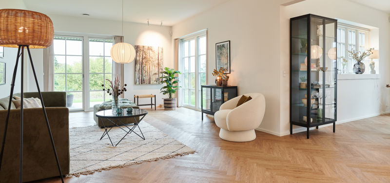 Lyst stueområde fra eurodan-huse med rund loungestol, sort vitrineskab, stor glasdør mod terrasse, rund pendellampe, vægkunst og naturligt lys fra flere sider – inspiration til palæstil, nybyggeri og åbne husdrømme.