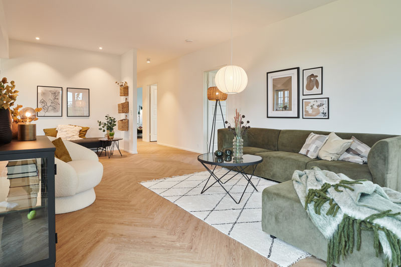 Stue fra eurodan-huse med grøn hjørnesofa, cremefarvet loungestol, sort rundt sofabord, hvidt tæppe med grafisk mønster, billedvæg over sofaen og varm belysning i rummet – inspiration til nybyggeri, husbyggeri og moderne husdrømme.