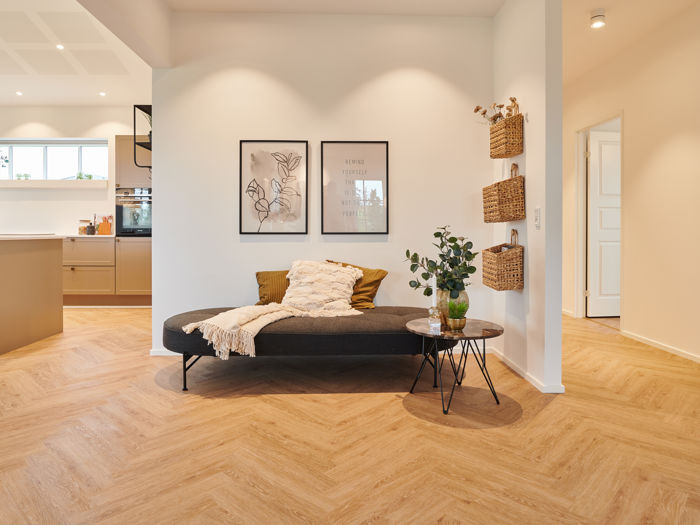 Hyggelig opholdskrog i moderne vinkelhus med daybed, sildebensgulv og kig mod køkkenet – inspiration til indretning af nybyg og drømmehuset.