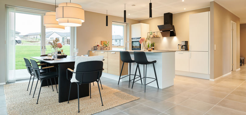 Åbent køkken-alrum i nybyggeri med køkkenø, spiseplads, store vinduespartier og moderne belysning – inspiration til familiens husdrømme.