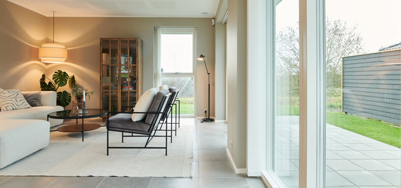Lys og moderne stue i nybyggeri med store gulv-til-loft-vinduer, terrasseadgang og stilren indretning – inspiration til personlige husdrømme.