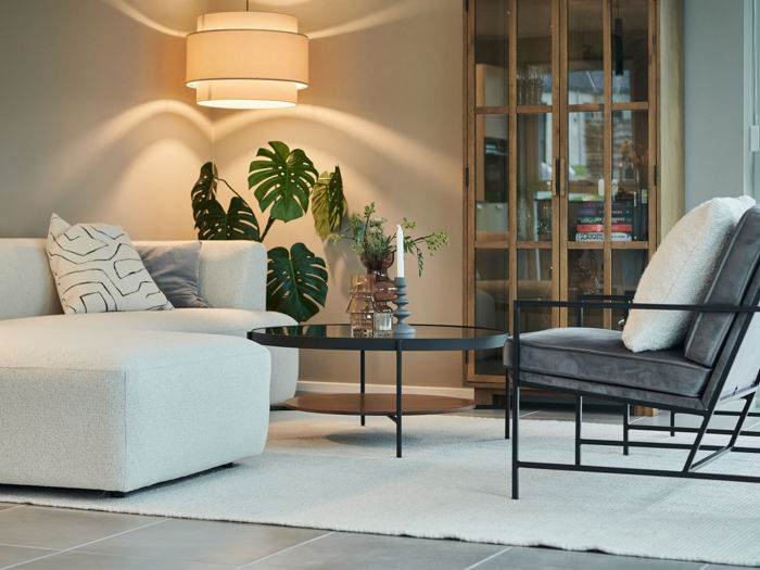 Stilren stue i nybyggeri med lys sofa, loungestol, grønne planter, rundt sofabord og moderne belysning