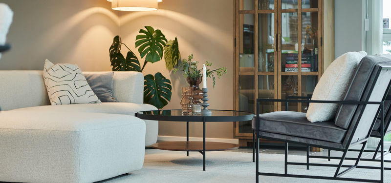 Stilren stue i nybyggeri med lys sofa, loungestol, grønne planter, rundt sofabord og moderne belysning