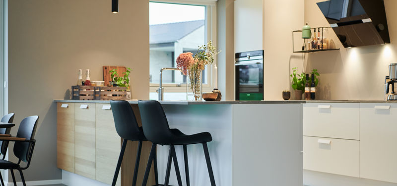 Moderne køkken i nybyggeri med køkkenø, barstole, ovenlys og stilrene hvide fronter – inspiration til funktionelle husdrømme.