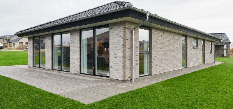 Moderne længehus i nybyggeri med lys murstensfacade, valmtag, store vinduespartier og terrasse – inspiration til familiens husdrømme.