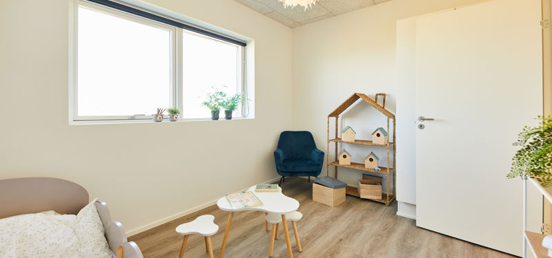 Lyst børneværelse i nybyggeri med legehjørne, børnemøbler, stort vindue og hyggelig indretning – inspiration til et funktionelt familiehjem.