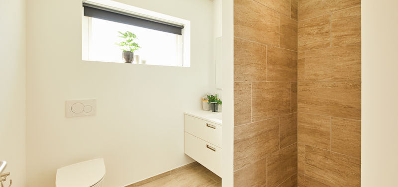 Moderne badeværelse i nybyggeri med væghængt toilet, svævende vaskemøbel, stort vindue og bruseniche med trælook-fliser – inspiration til stilrent husbyggeri.