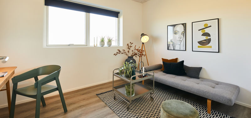 Hyggeligt multirum i nybyggeri med sofa, arbejdsplads, stort vindue og moderne indretning – inspiration til fleksible rum i boligen.