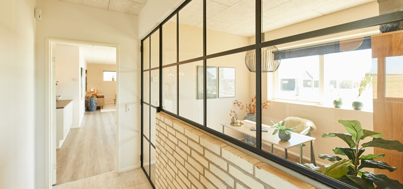 Indvendig glasvæg med sorte sprosser og muret brystning i moderne nybyggeri – en stilren rumdeler, der skaber lys og åbenhed i boligen.