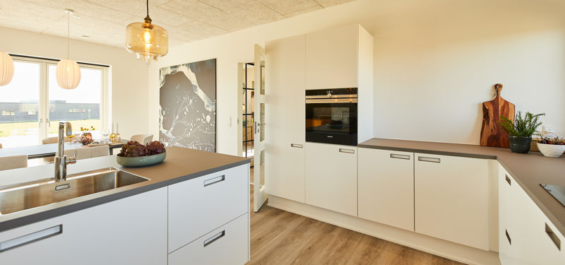 Moderne køkken i nybyggeri med lyse fronter, køkkenø, trælook-gulv og integrerede hvidevarer – inspiration til stilrent husbyggeri.