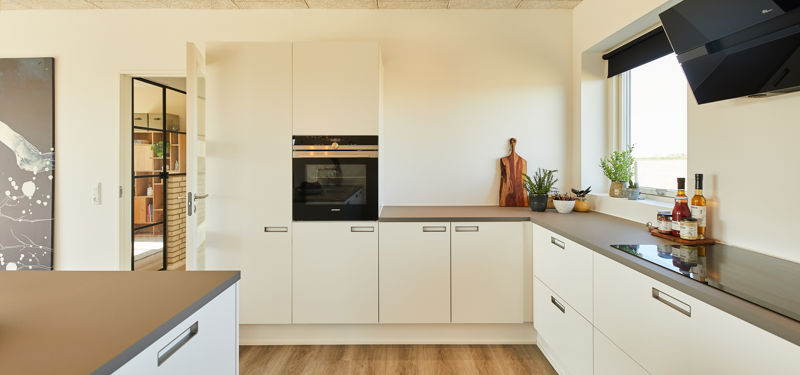 Stilrent køkken i nybyggeri med lyse fronter, mørk bordplade, integrerede hvidevarer og trælook-gulv – moderne inspiration til husbyggeri.