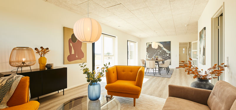 Lys og moderne stue i nybyggeri med farverige loungemøbler, store vinduer og åben forbindelse til spiseområdet – inspiration til personligt husbyggeri.
