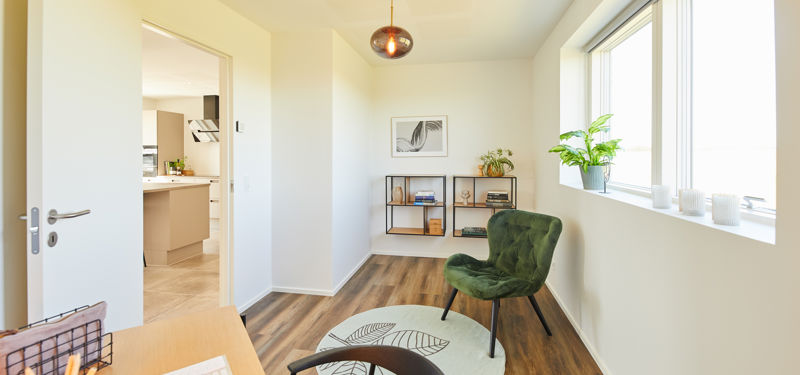Indbydende hjemmekontor med træskrivebord, grøn loungestol, små reoler og stort vindue – funktionel inspiration til drømmehuset.