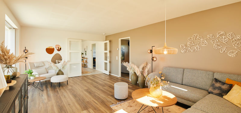 Separat stue med to sofaområder, varme jordfarver, gulv i trælook og store vinduespartier – hyggelig indretning til et moderne nybyg.