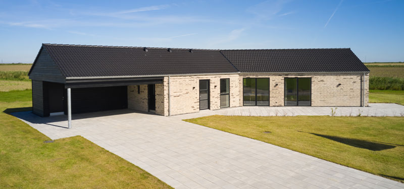 Knækhus på 155 m² med integreret carport, lys facade, sort tag og stor flisebelagt indkørsel – inspiration til nybyggerdrømme.