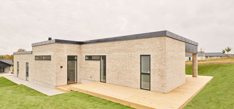Nybygget funkisvilla fra eurodan-huse med lang lys murstensfacade, sorte vinduesrammer og træterrasse til moderne husbyggeri
