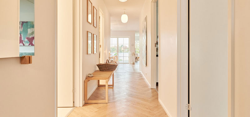 Lys gang i nyt hus med sildebensgulv og kig gennem boligen mod søen.