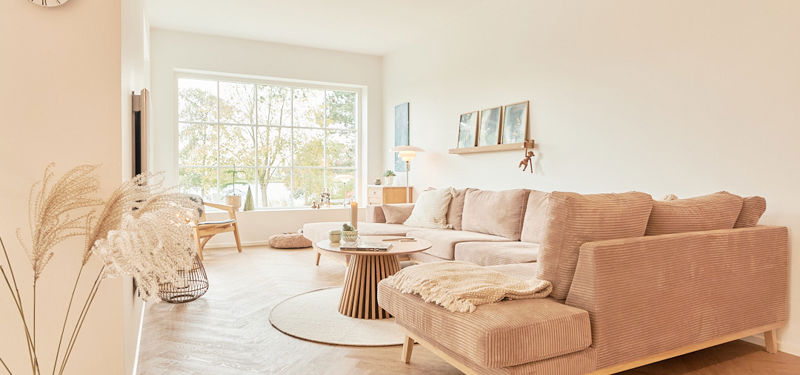 Lys stue i Maiken og Johnnys drømmehus med stor sofa og sprosset vindue mod naturen.