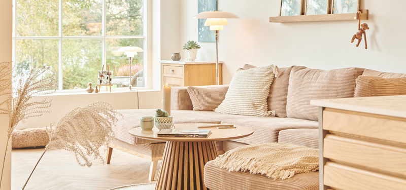 Moderne stue i nybyg med stor sofa, varme naturmaterialer og udsigt gennem vinduet.