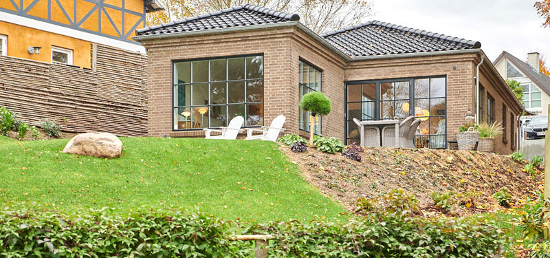 Nybygget murstenshus i Hornbæk med store sorte vinduespartier og kuperet have.