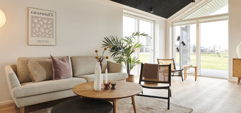 Lys stue i moderne nybyggeri med loft til kip, sort akustikloft, store gulv-til-loft-vinduer og direkte udgang til haven – inspiration til stilrene husdrømme.