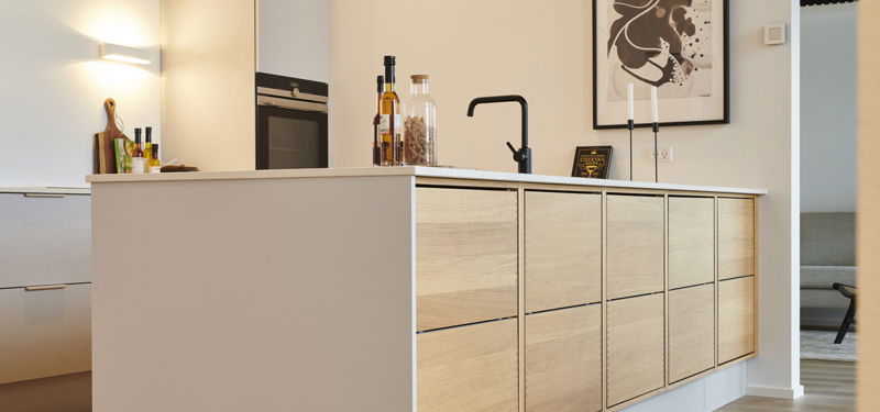 Moderne køkkenø med fronter i lyst træ, hvid bordplade, sort vask og armatur samt rummelige skuffer – stilren inspiration til nybyg og familiens husdrømme.