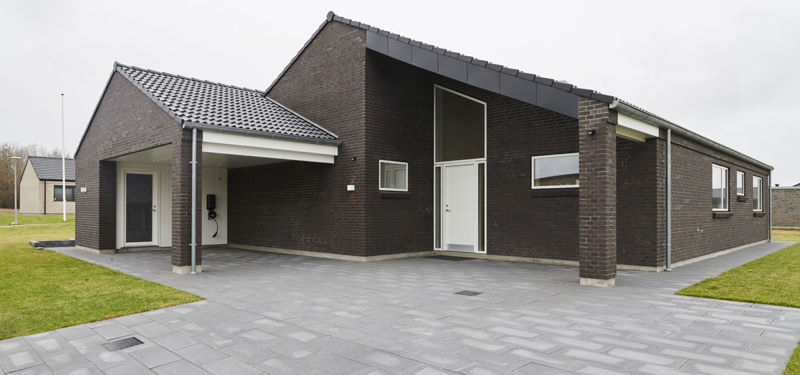 Overdækket carport ved mørk murstensfacade med sort tegltag, højt indgangsparti, brede grå fliser og flere tagudhæng omkring huset – inspiration til carport, garagevalg og moderne nybyggeri fra eurodan-huse.