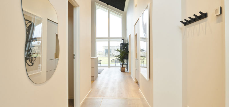 Lys entré fra eurodan-huse med store gulvfliser, organisk spejl, sort knagerække, højt loft, store vinduespartier og kig videre mod opholdsrum – inspiration til rummelig entré, nybyggeri og moderne husbyggeri.
